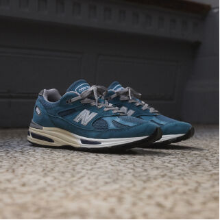 A pair of New Balance Made in UK sneakers sitting on a concrete floor.