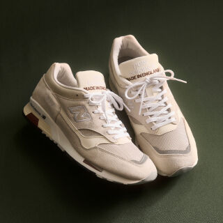 A pair of New Balance Made in UK sneakers on a green textured studio environment. 