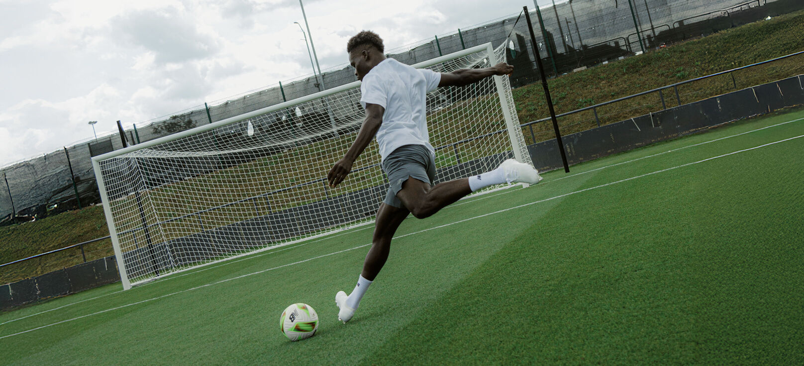 bukayo saka kicking a football ball to an emty goal with new balance football boots