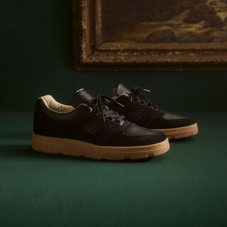 Knee down view of a man wearing a pair of New Balance Made in UK sneakers standing on a patterned tile floor.  