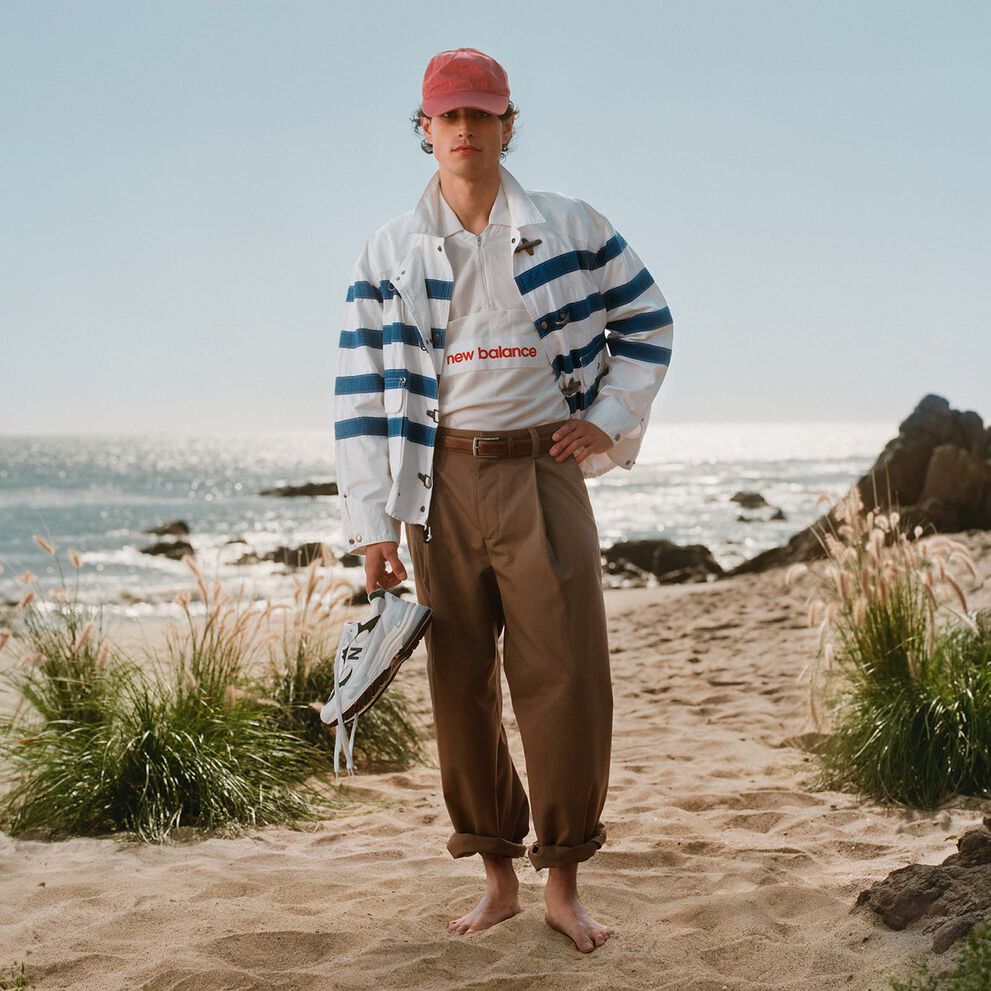 A man standing on a beach holding a pair of shoes. 