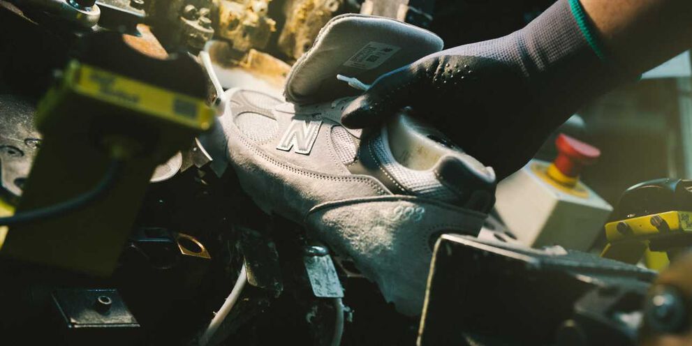 A hand putting a New Balance shoe in a device in a factory environment.